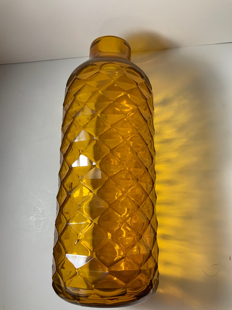 May include: A tall, amber glass vase with a diamond-shaped pattern. The vase is empty and has a rounded bottom.