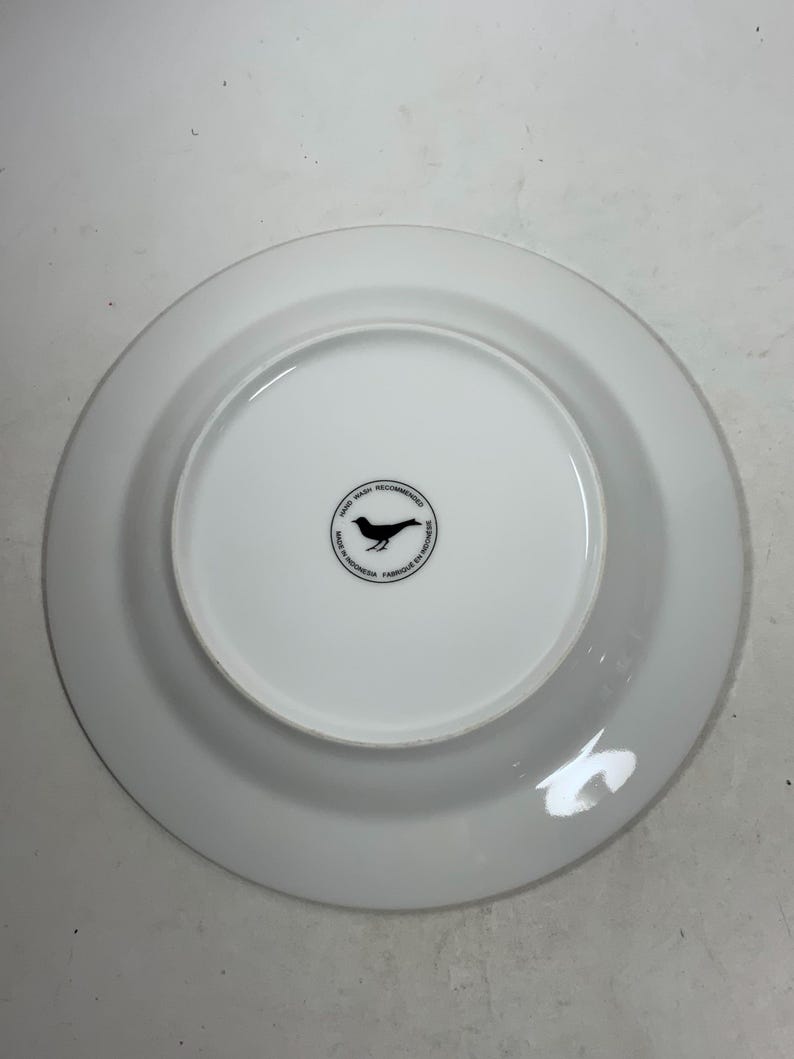 May include: White ceramic plate with a black bird logo that reads "Hand Wash Recommended Made in Indonesia Fabriqu&eacute; en Indon&eacute;sie".