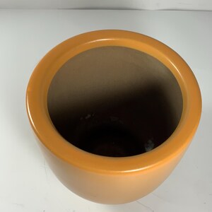Pu&ograve; includere: Un grande vaso rotondo in ceramica arancione con una finitura liscia e lucida.