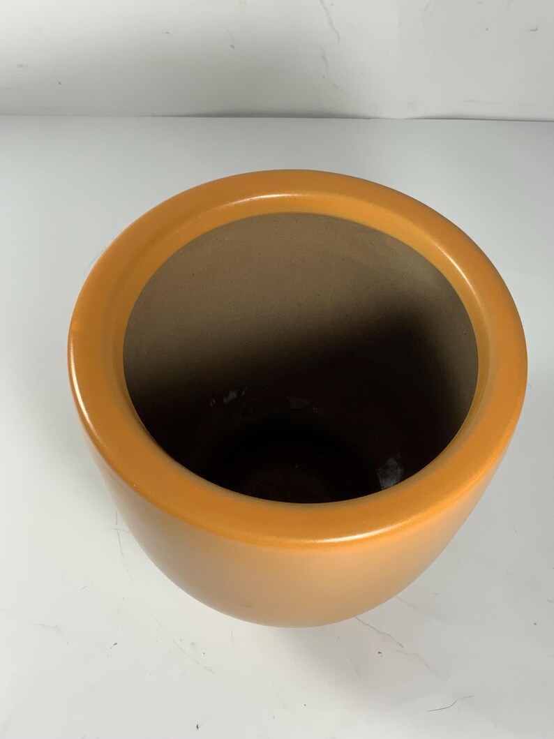 Pu&ograve; includere: Un grande vaso rotondo in ceramica arancione con una finitura liscia e lucida.