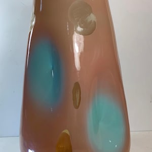 May include: A tall, teardrop-shaped vase in shades of peach and brown, with large teal and beige abstract shapes. The glossy surface reflects light, highlighting the smooth curves of the decorative glass vessel.