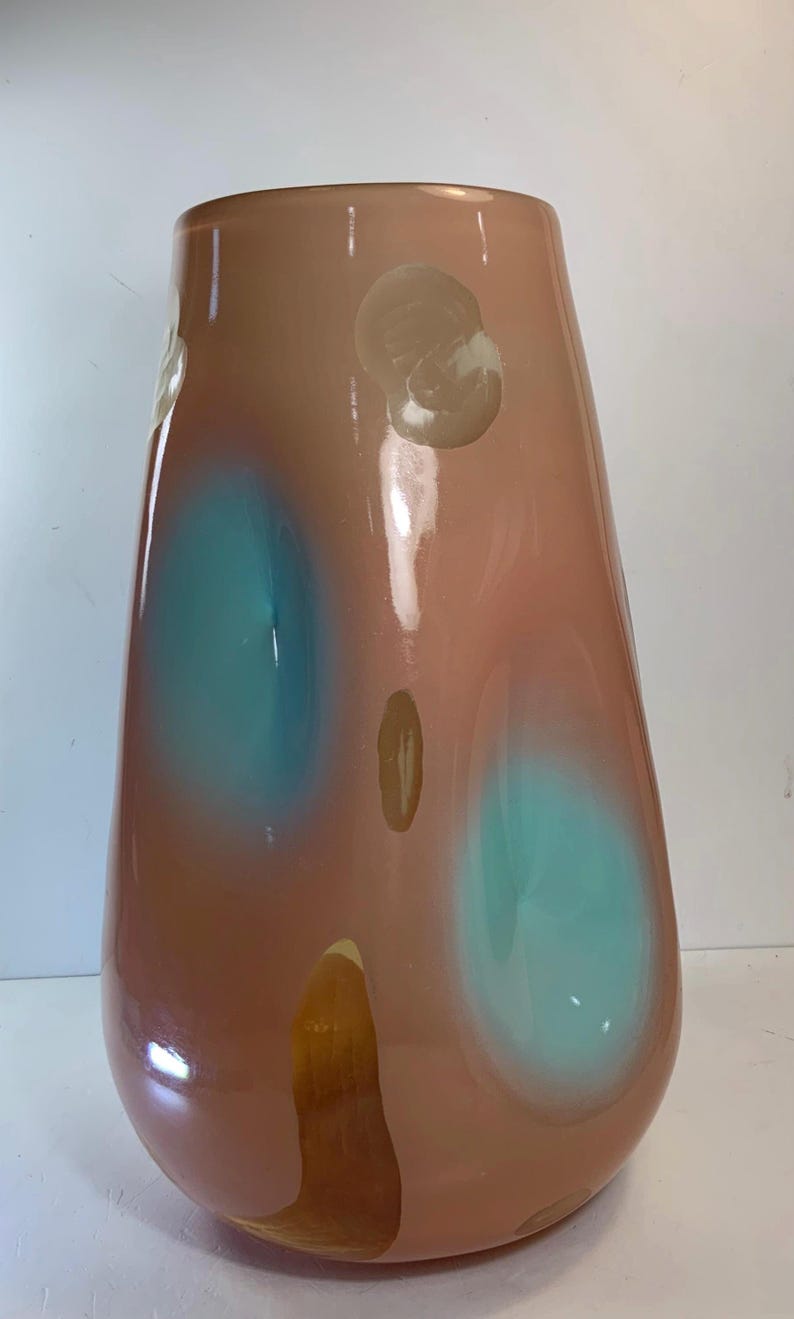 May include: A tall, teardrop-shaped vase in shades of peach and brown, with large teal and beige abstract shapes. The glossy surface reflects light, highlighting the smooth curves of the decorative glass vessel.