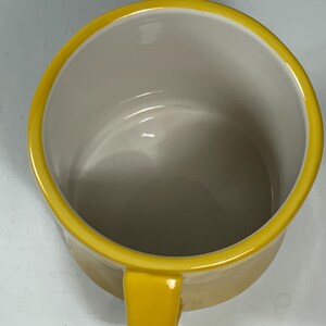 Puede incluir: Una taza de cer&aacute;mica amarilla con un asa a juego y un borde amarillo. El interior de la taza es de color beige claro. La taza est&aacute; vac&iacute;a y parece limpia.