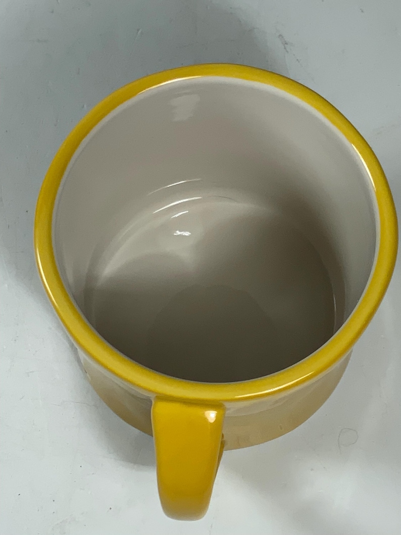 Puede incluir: Una taza de cer&aacute;mica amarilla con un asa a juego y un borde amarillo. El interior de la taza es de color beige claro. La taza est&aacute; vac&iacute;a y parece limpia.