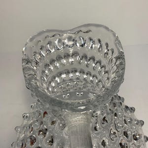 May include: Clear glass pitcher with a textured, bubble-like pattern. The pitcher has a heart-shaped opening and a handle. The glass is transparent, allowing light to pass through, and the design adds visual interest.