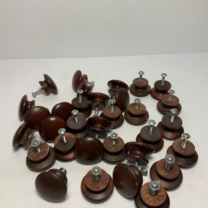 May include: A collection of dark brown wooden cabinet knobs with attached screws. The knobs vary in shape, including round, oval, and mushroom styles. Some knobs are assembled with multiple wooden layers.