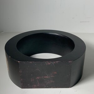 Puede incluir: Un anillo de madera negro con una forma octogonal ligeramente redondeada. El anillo tiene un di&aacute;metro de aproximadamente 25 cm y una altura de 7,5 cm.