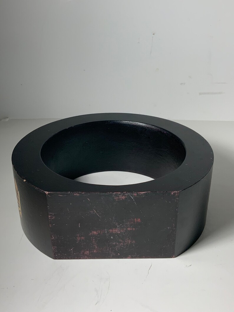 Puede incluir: Un anillo de madera negro con una forma octogonal ligeramente redondeada. El anillo tiene un di&aacute;metro de aproximadamente 25 cm y una altura de 7,5 cm.