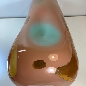 May include: A tall, teardrop-shaped vase with a peach-colored body. The vase features irregular brown and gold accents, with a central turquoise-colored area. The glass vase has a glossy finish and a wide base.
