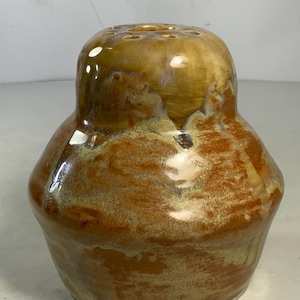 以下が含まれることがあります： 茶色と黄色の釉薬をかけた陶器の花瓶。花瓶は幅広の底と、花茎用の穴が複数開いた細い首を持つ。