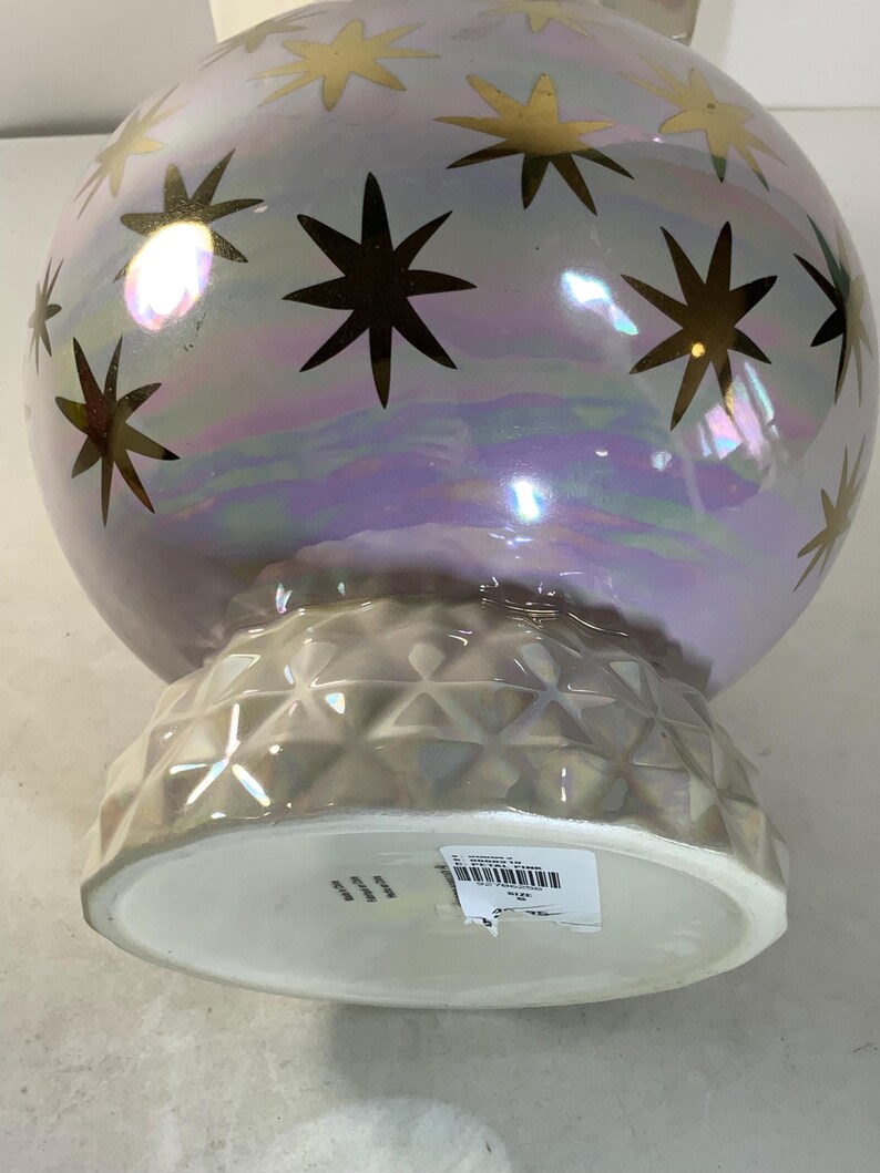 May include: A pearlescent, spherical decorative vase with gold star accents. The vase has a textured, geometric base and a wide, white opening. The iridescent finish reflects a range of colors, creating a celestial aesthetic.