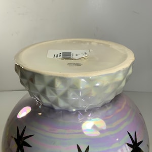 May include: Iridescent decorative vase with a round base and a textured, geometric top. The vase features gold starburst designs. The bottom of the vase is a pearlescent purple, and the top is a light gray.