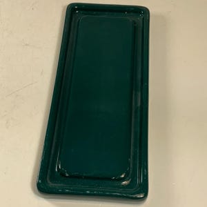 May include: A rectangular, dark green metal tray with a raised edge. The tray has a glossy finish and a slightly worn appearance. The design is simple and functional, suitable for serving or organizing items.