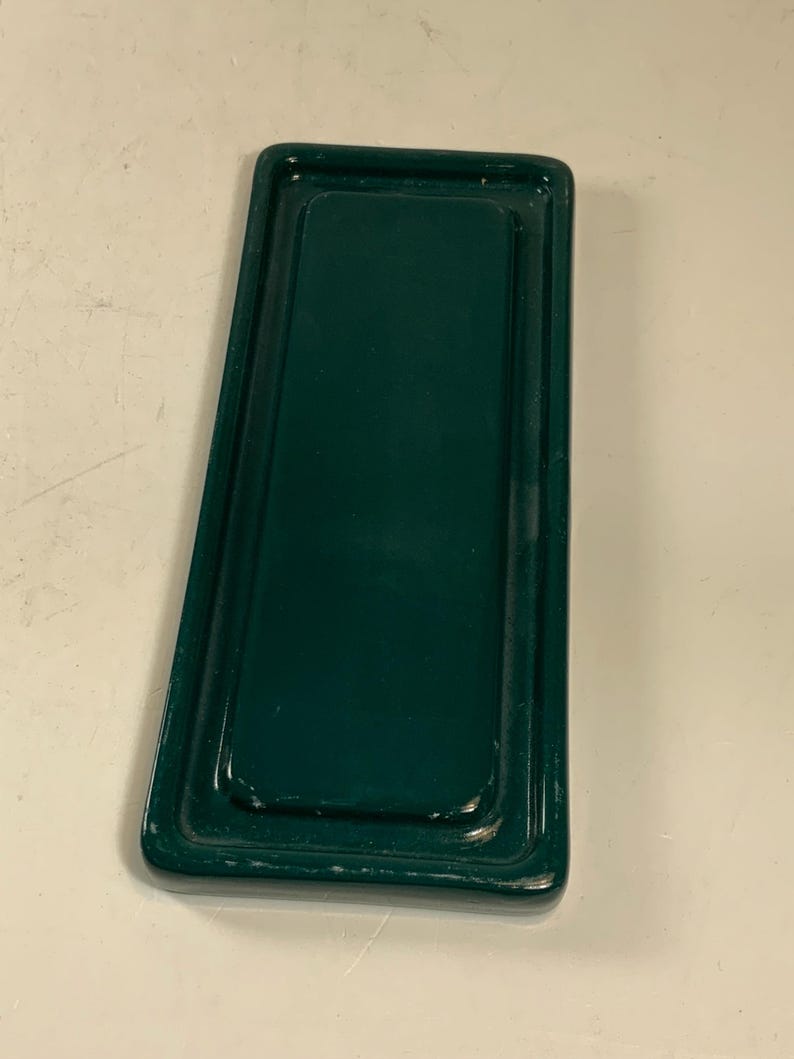 May include: A rectangular, dark green metal tray with a raised edge. The tray has a glossy finish and a slightly worn appearance. The design is simple and functional, suitable for serving or organizing items.