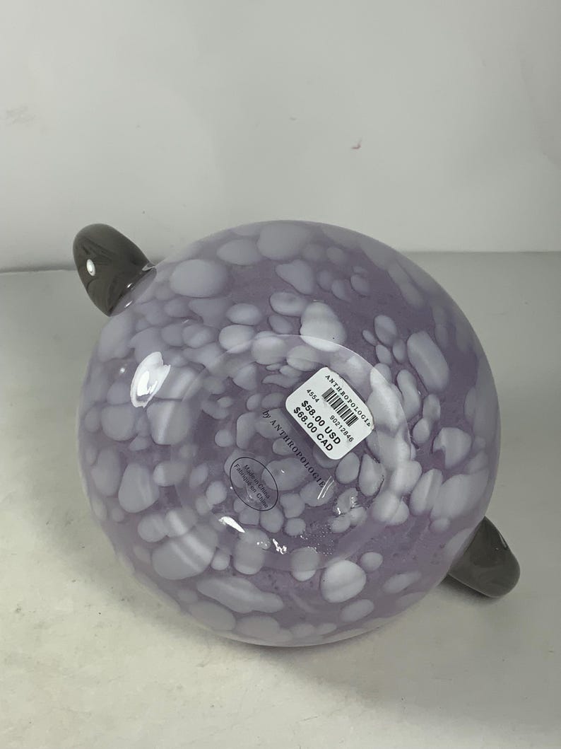 May include: Purple glass bowl with white polka dots and two grey handles. The bowl has a price tag attached that reads "&pound;58.00 USD &pound;68.00 CAD" and "Anthropologie".