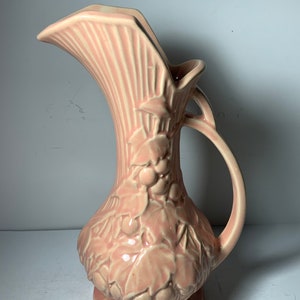 May include: A pink ceramic pitcher with a wide, flared spout and a handle. The pitcher is decorated with a raised design of leaves and grapes.