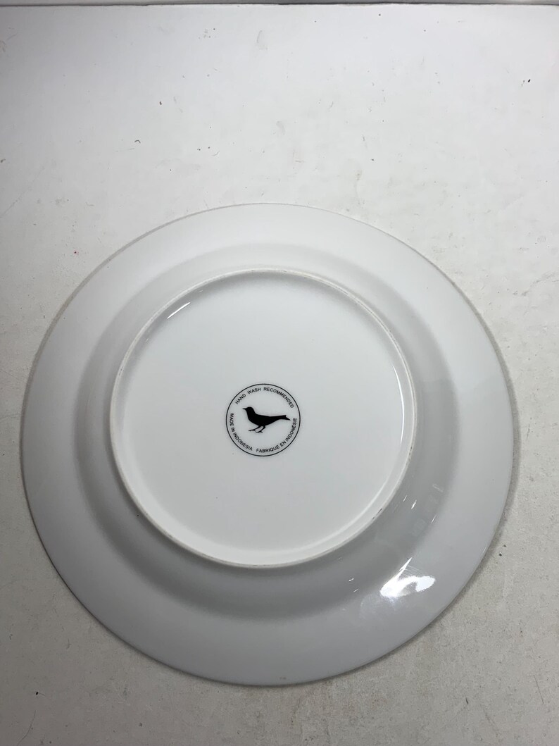 May include: White ceramic plate with a black bird logo on the bottom. The logo says "Hand Wash Recommended" and "Made in Indonesia - Fabriqu&eacute; en Indon&eacute;sie".