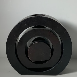 Puede incluir: Una escultura de madera negra con tres c&iacute;rculos conc&eacute;ntricos. La escultura est&aacute; hecha de tres piezas de madera separadas que est&aacute;n apiladas una encima de la otra.