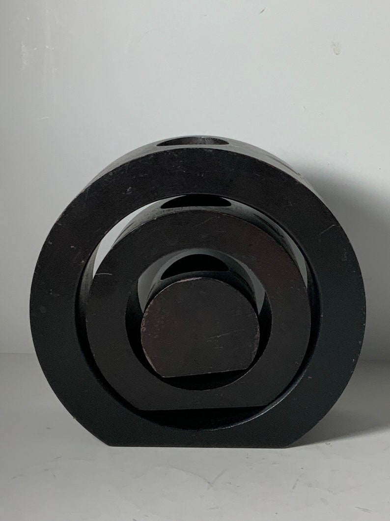 Puede incluir: Una escultura de madera negra con tres c&iacute;rculos conc&eacute;ntricos. La escultura est&aacute; hecha de tres piezas de madera separadas que est&aacute;n apiladas una encima de la otra.