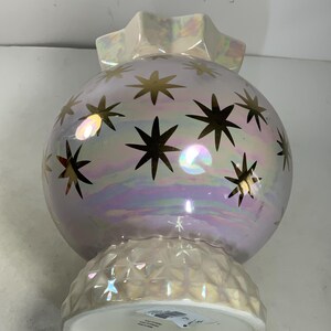 May include: Iridescent decorative orb-shaped vase with gold star accents. The vase has a ruffled top and a textured base. The pearlescent finish reflects light, creating a shimmering effect. A unique home decor item.