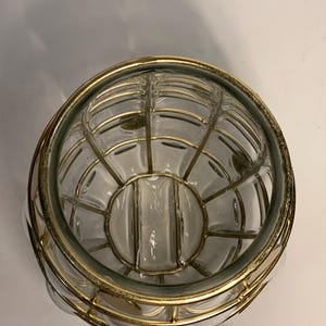 Op de afbeelding: Transparante glazen kom met een goudkleurig metalen kooi-ontwerp. De kom heeft een afgeronde vorm met een decoratieve metalen rand. Het kooi-ontwerp voegt een vintage of antieke esthetiek toe.