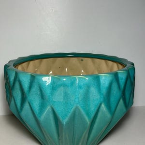 May include: A turquoise ceramic bowl featuring a geometric diamond-shaped faceted exterior pattern. The bowl has a glossy finish on the outside and a smooth, light beige interior surface. The rim is circular with a scalloped edge design.