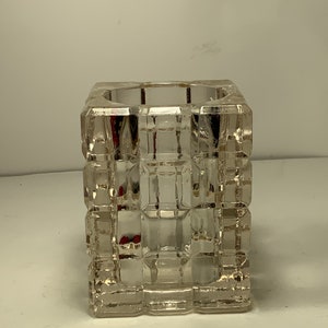 Op de afbeelding: Een vierkante kaarsenhouder van helder glas met een geometrisch patroon. De houder is gemaakt van dik glas en heeft een gladde, gepolijste afwerking.