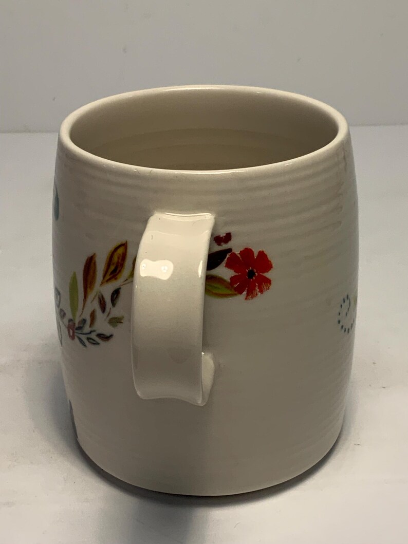 Puede incluir: Taza de cer&aacute;mica color crema con dise&ntilde;o floral. La taza tiene un asa blanca y est&aacute; adornada con patrones florales rojos, marrones y verdes. La taza tiene forma cil&iacute;ndrica y una superficie texturizada.