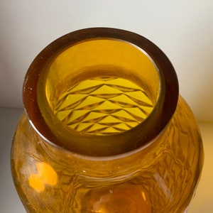 May include: Amber glass vase with a geometric pattern on the inside. The vase has a wide mouth and a rounded body.