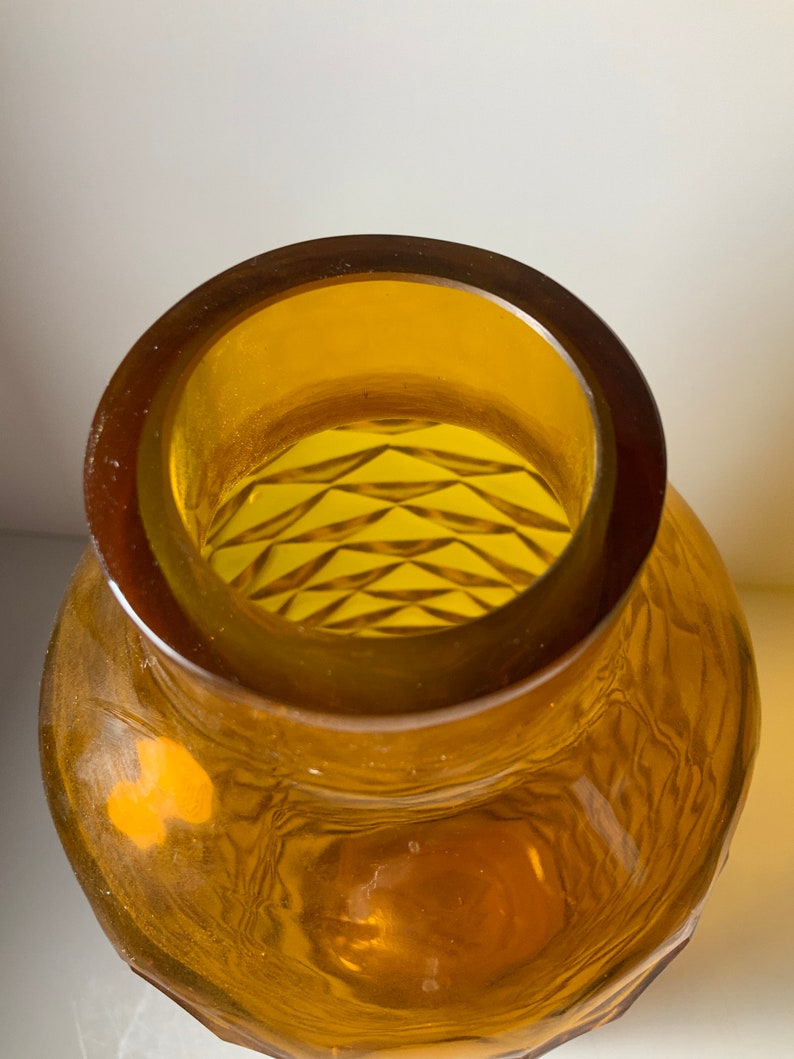 May include: Amber glass vase with a geometric pattern on the inside. The vase has a wide mouth and a rounded body.