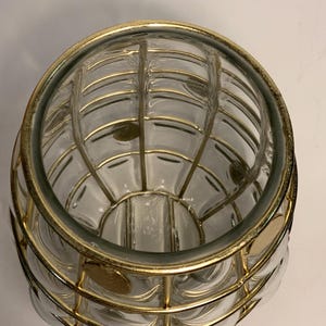 Op de afbeelding: Een heldere glazen vaas met een gouden metalen kooi-ontwerp. De vaas heeft een ronde vorm met een reeks heldere, belachtige glazen secties. De gouden metalen kooi wikkelt zich om het glas en cre&euml;ert een decoratief patroon.