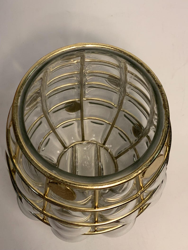 Op de afbeelding: Een heldere glazen vaas met een gouden metalen kooi-ontwerp. De vaas heeft een ronde vorm met een reeks heldere, belachtige glazen secties. De gouden metalen kooi wikkelt zich om het glas en cre&euml;ert een decoratief patroon.