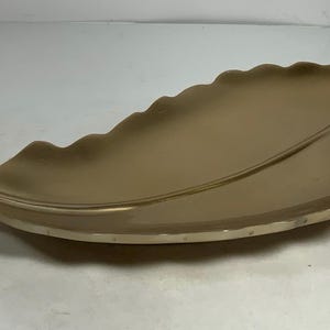 Puede incluir: Una bandeja de servir dorada en forma de hoja con un acabado liso y met&aacute;lico. La bandeja est&aacute; dise&ntilde;ada para parecerse a una hoja grande con una forma ligeramente curvada.