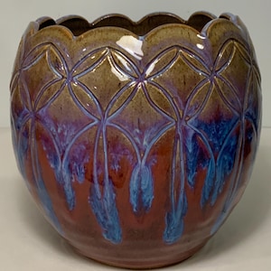 May include: A handcrafted ceramic bowl with a scalloped rim. The bowl features a geometric pattern and a blend of colors, including brown, purple, and blue. The bowl's exterior has a glossy finish, and the interior is a darker shade of brown.
