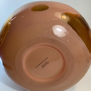May include: A peach-colored, round decorative bowl with gold accents. The bowl has a wide base and a rounded top. The bottom of the bowl has the text "by ANTHROPOLOGIE Made in India Fabriqu&eacute; en Inde."