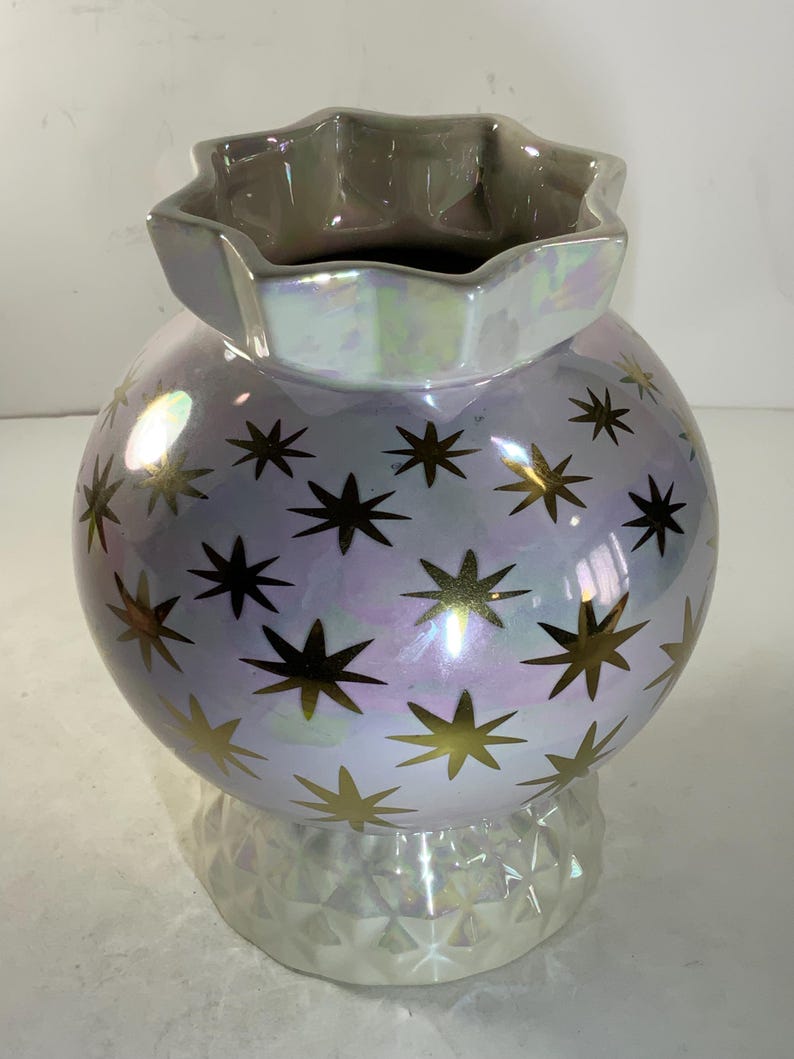 May include: A pearlescent ceramic vase with a spherical body and a star-shaped opening. The vase is decorated with gold star patterns. The base has a geometric design. The vase is approximately 8 inches tall.
