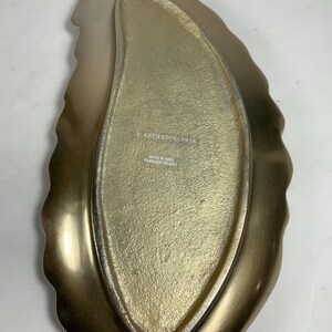 Puede incluir: Bandeja de servir dorada en forma de hoja con borde festoneado. La bandeja est&aacute; hecha en India y tiene el logotipo de Anthropologie en la parte inferior.