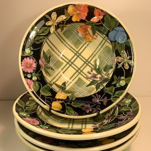 Puede incluir: Un juego de cuatro platos decorativos de cerámica. Cada plato presenta un borde negro con diseños florales y de libélulas. El centro de cada plato tiene un patrón de cuadros verdes y amarillos. Los platos están apilados.