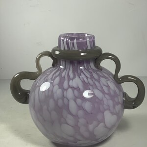 May include: A purple glass vase with white speckles and grey handles. The vase has a round body and a wide opening.