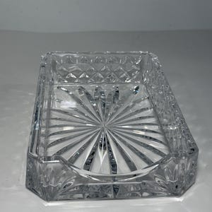 May include: A rectangular clear glass tray featuring a faceted diamond pattern along the exterior walls and a sunburst design radiating from the centre of the base. The front edge of the tray has a shallow, curved cutout for easy access.