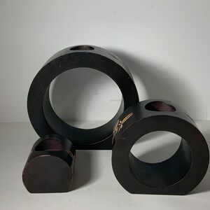 Puede incluir: Tres candelabros de madera negra de diferentes tama&ntilde;os. El candelabro m&aacute;s grande es de forma de anillo con un agujero en el centro. El candelabro del medio es de forma de anillo con un agujero en el centro y un dise&ntilde;o decorativo. El candelabro m&aacute;s peque&ntilde;o es un peque&ntilde;o cilindro con un agujero en el centro.