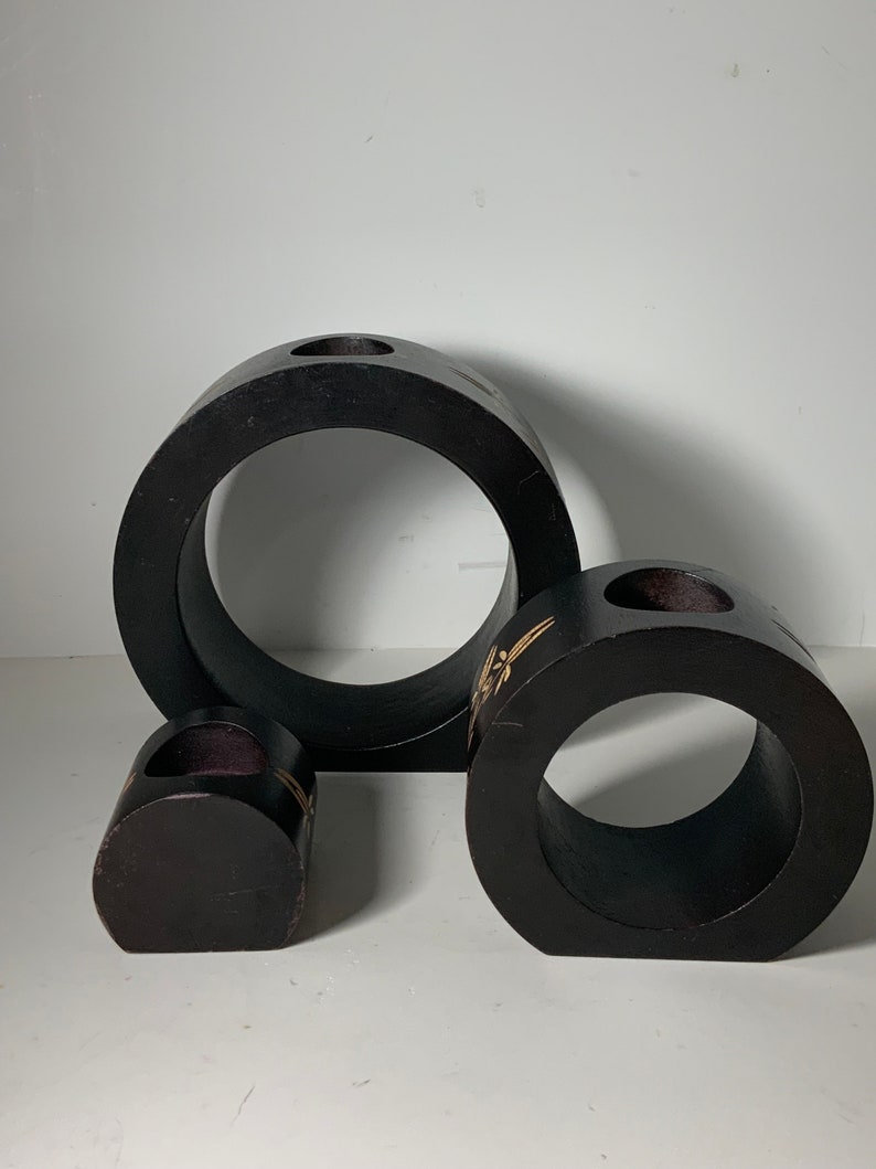 Puede incluir: Tres candelabros de madera negra de diferentes tama&ntilde;os. El candelabro m&aacute;s grande es de forma de anillo con un agujero en el centro. El candelabro del medio es de forma de anillo con un agujero en el centro y un dise&ntilde;o decorativo. El candelabro m&aacute;s peque&ntilde;o es un peque&ntilde;o cilindro con un agujero en el centro.
