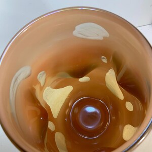 May include: A decorative glass vase with a unique, organic shape. The vase features a warm, amber color with creamy white accents. The interior has a glossy finish, and the overall design is modern and artistic.