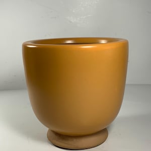 Pu&ograve; includere: Un vaso da fiori in ceramica color terracotta con corpo arrotondato e base larga e piatta.