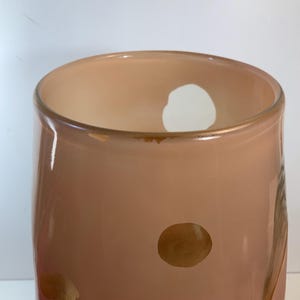 May include: A peach-colored glass vase with a cylindrical shape. The vase has a wide opening and a few brown spots on the surface. The background is white.