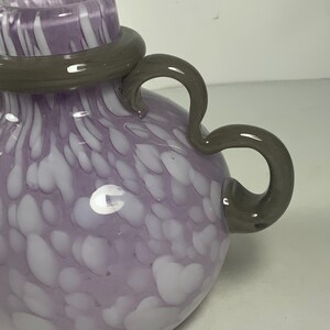 May include: A purple and white glass vase with a grey handle. The vase has a swirling pattern of white on a purple background.