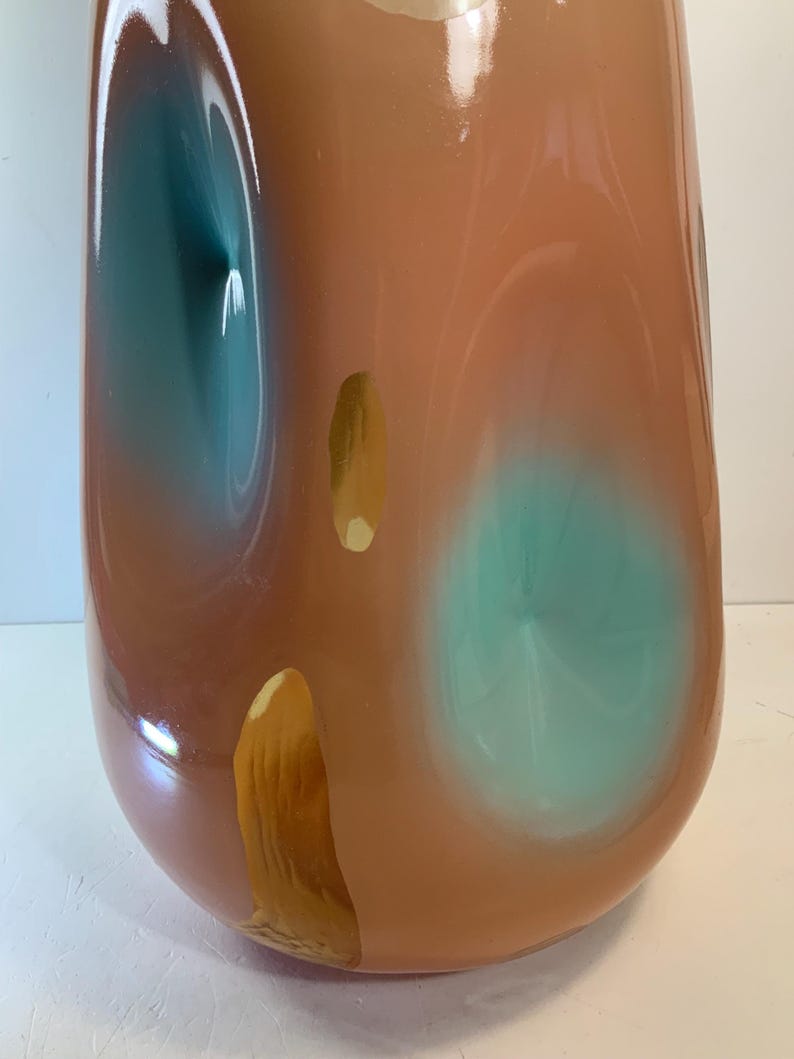 May include: A tall, rounded vase with a glossy finish. The vase features a blend of colors, including peach, teal, and gold. Teal and gold accents are layered over the peach base, creating an abstract design. The vase has a smooth, curved shape.