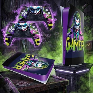 Op de afbeelding: Een gameconsole en controllers met een Joker-thema. De controllers zijn zwart met een Joker-gezichtsontwerp en paarse, groene en gele accenten. De console heeft een paarse voorkant met een Joker-afbeelding en het woord "GAMER".