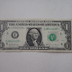 May include: A one dollar bill with a portrait of George Washington. The bill has the serial number E00414100 and is signed by the Treasurer of the United States,  J.  J.  Garrangue, and the Secretary of the Treasury, Steven T.  Mnuchin.