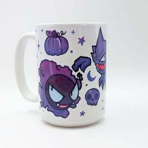 May include: A white ceramic mug featuring a purple graphic print of a round ghost-like creature with large eyes, a small skull, a pumpkin, a crescent moon, and several small stars scattered across the surface of the drinkware item.